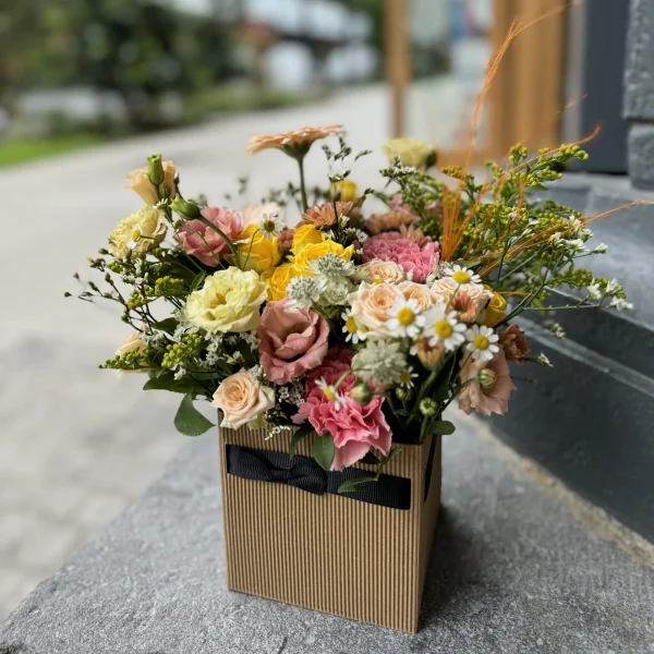 Arrangement floral Le Cubique, composé de fleurs frâiches dans les tons rose et jaune selon fleurs de saison